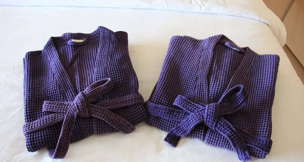 Due accappatoi viola, piegati e legati con la loro cintura, pronti per essere riposti. Ecco come piegare un accappatoio per un riordino perfetto.