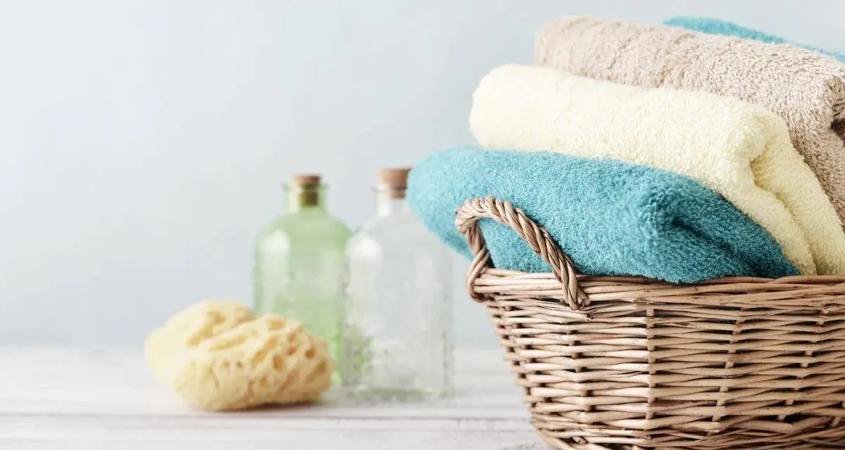 Cesto di vimini con asciugamani morbidi, come i rimedi della nonna. Accanto, spugna naturale e bottiglie di vetro.