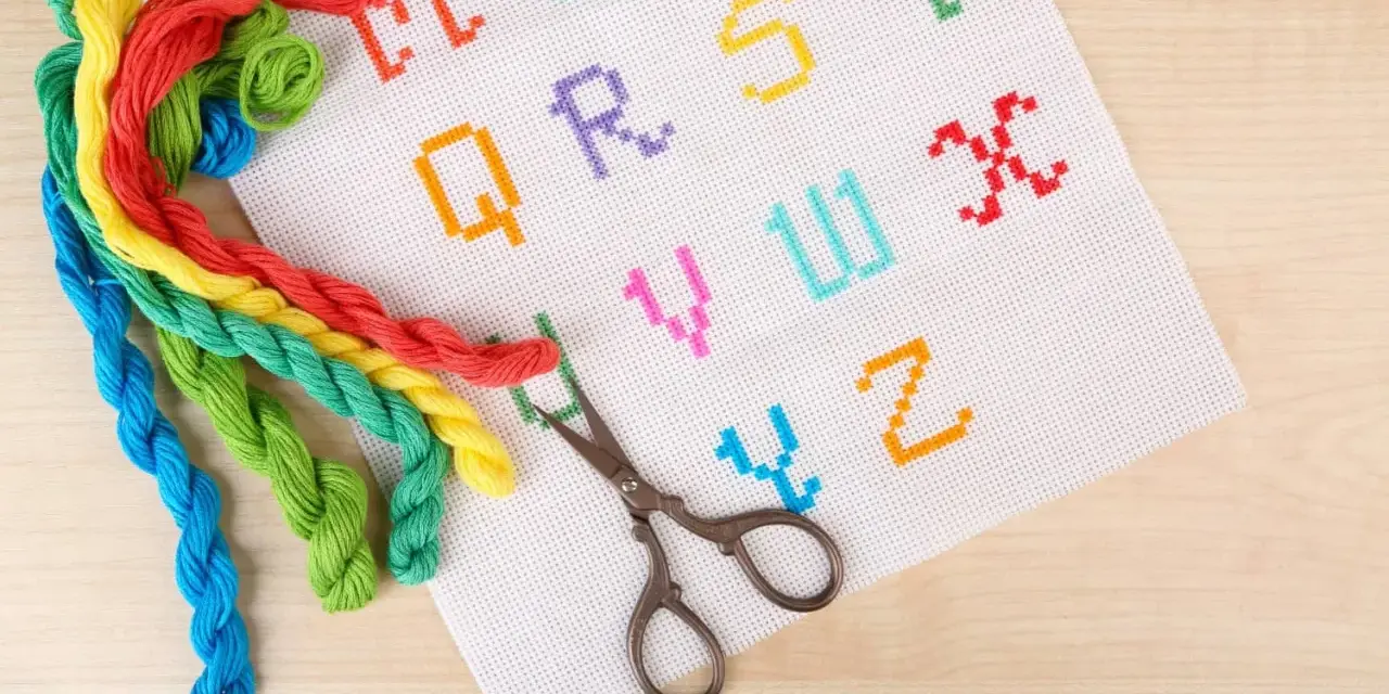 Fili colorati e forbicine pronti per ricamare nomi punto catenella su tela bianca con lettere dell'alfabeto.