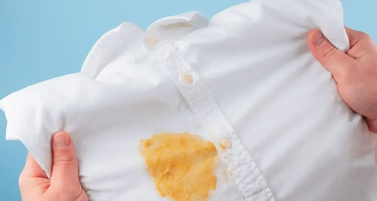 Come togliere le macchie gialle dalla biancheria colorata: una camicia bianca macchiata di giallo, tenuta in mano.