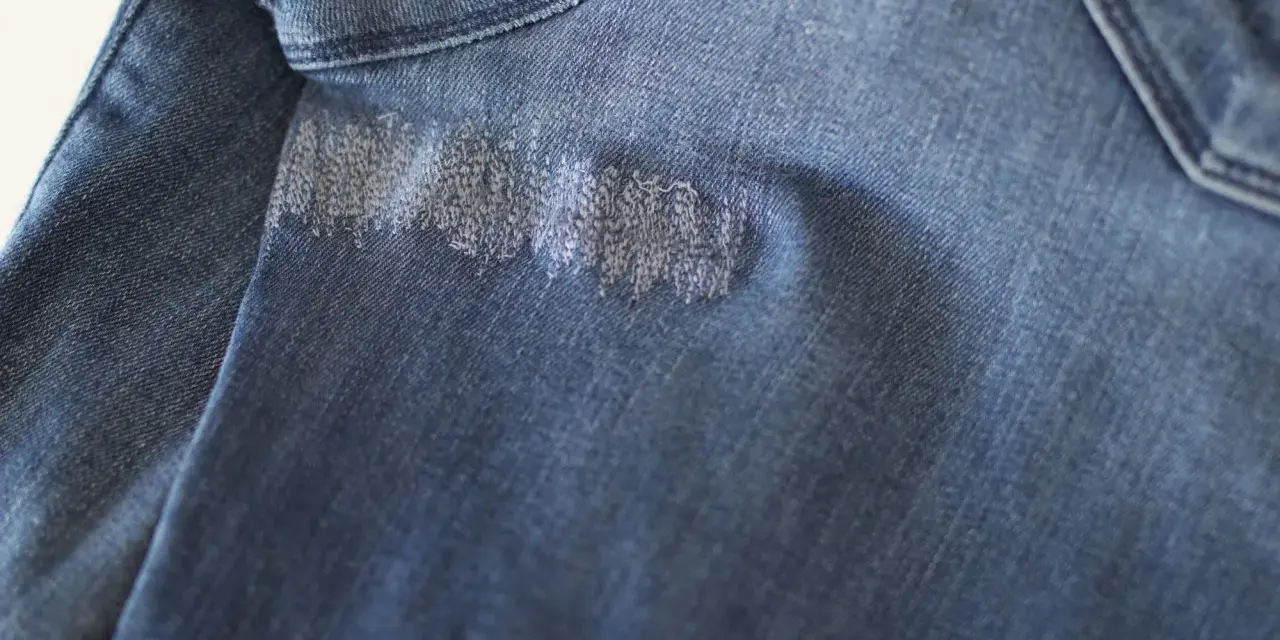 Dettaglio di un tessuto di jeans blu con un'area rattoppata con filo bianco, che mostra la cura nel rattoppare jeans.