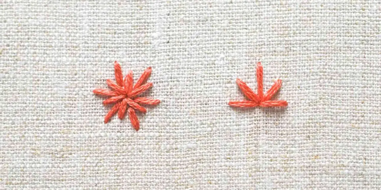 Two orange embroidery stitches on a textured linen fabric.