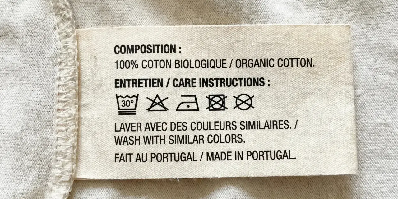 Etichetta con simboli tessuti: lavaggio 30°, non candeggiare, stirare a bassa temperatura, non lavare a secco, non asciugare in asciugatrice. 100% cotone biologico, fatto in Portogallo.