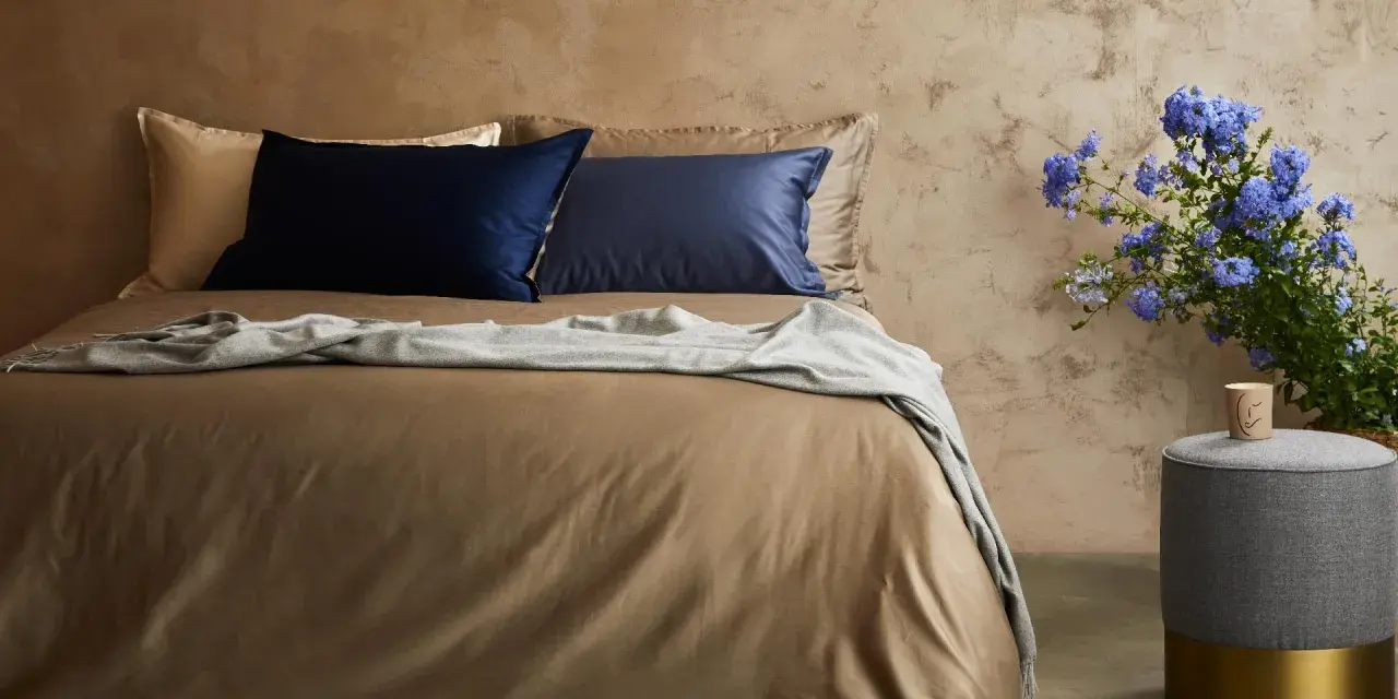 Letto con lenzuola color tabacco, cuscini blu e beige, coperta grigia. Il miglior tessuto per lenzuola per un sonno di qualità.