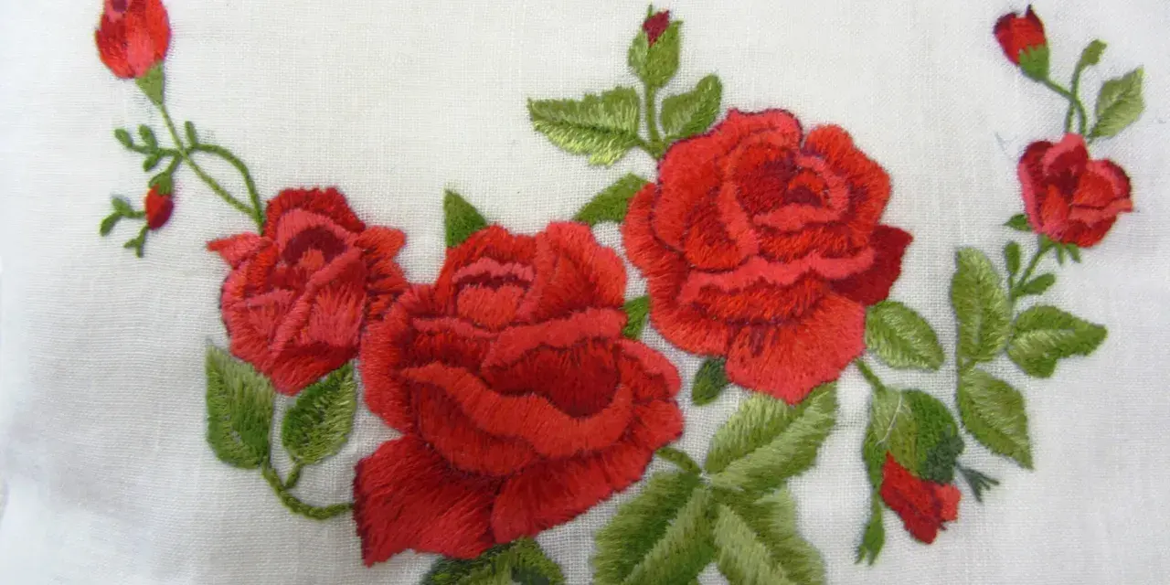 Ricamo di rose rosse su tessuto bianco, un delicato punto pittura che evoca un giardino fiorito.