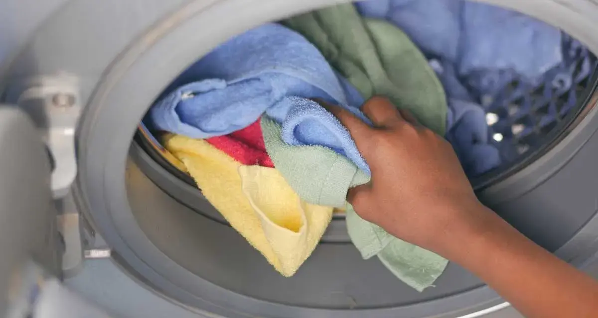 Mano inserisce asciugamani colorati in lavatrice. Scopri come lavare asciugamani in lavatrice per mantenerli morbidi e profumati.