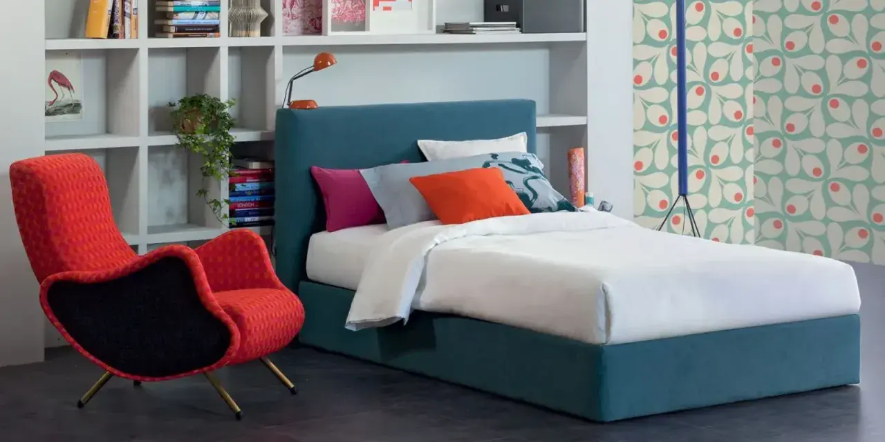 Letto una piazza e mezza con testiera blu, cuscini colorati e una poltrona rossa vivace.