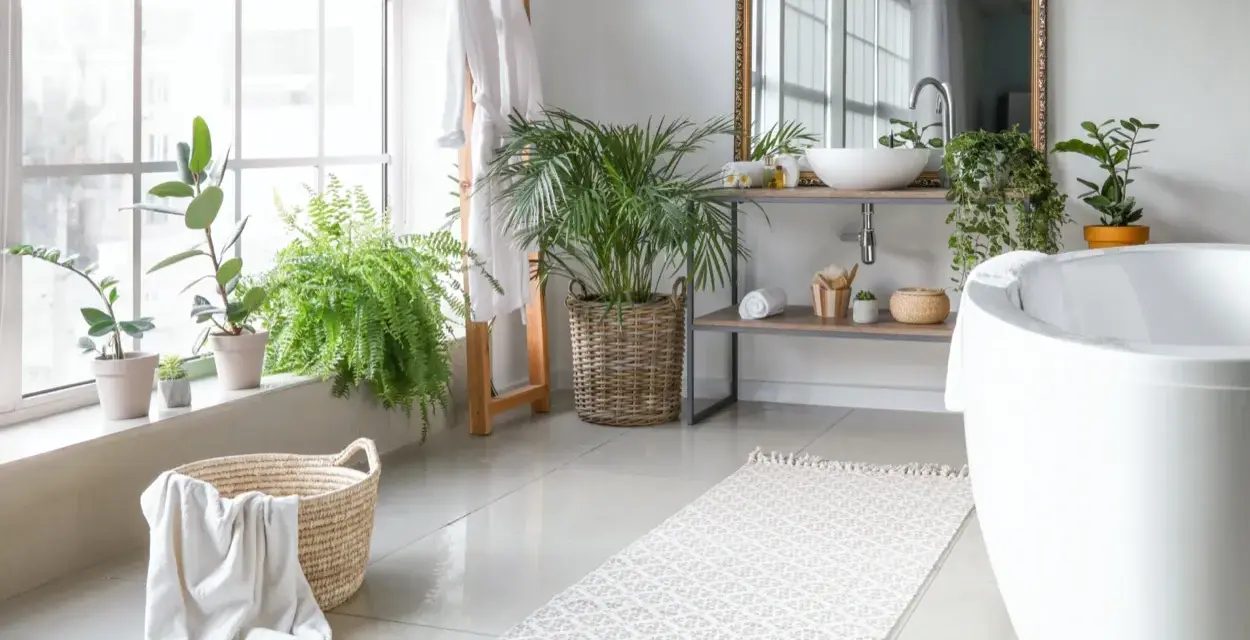 Bagno luminoso con piante, vasca, lavabo e un tappeto che aspetta di essere lavato in lavatrice.