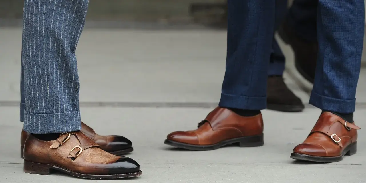 Primo piano su scarpe monk strap marroni e diversi tipi di orlo pantaloni: a risvolto e con pinces.