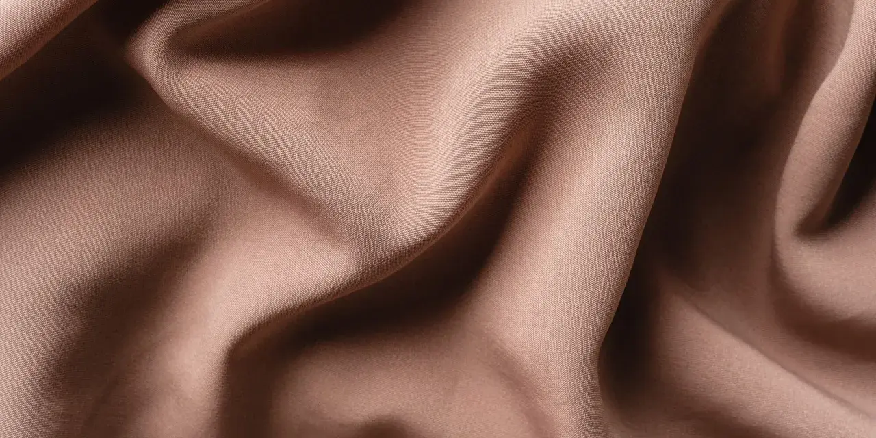Tessuto di raso color tortora, morbido e drappeggiato, che mostra la sua texture fine. Il raso si può stirare per ottenere una finitura impeccabile.