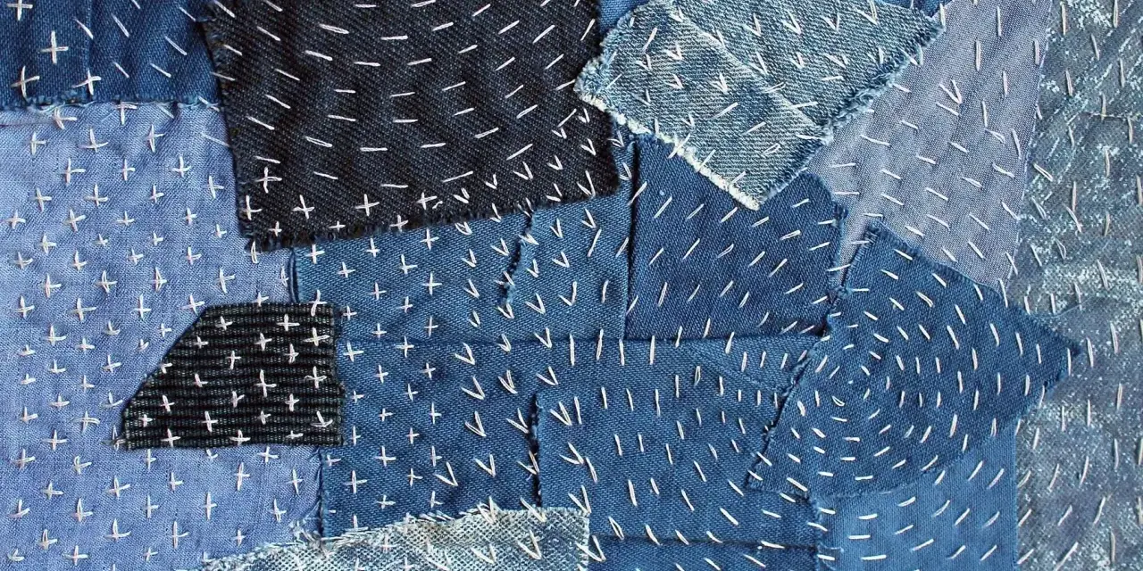 Tessuto patchwork in denim con cuciture bianche a punto croce e a zig-zag, un esempio di rammendo giapponese.