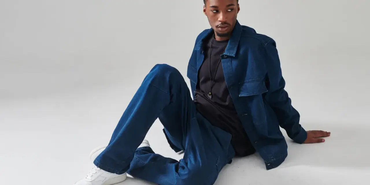 Un uomo con un completo di jeans blu, seduto a terra. Chissà quanto pesa un paio di jeans così comodi.