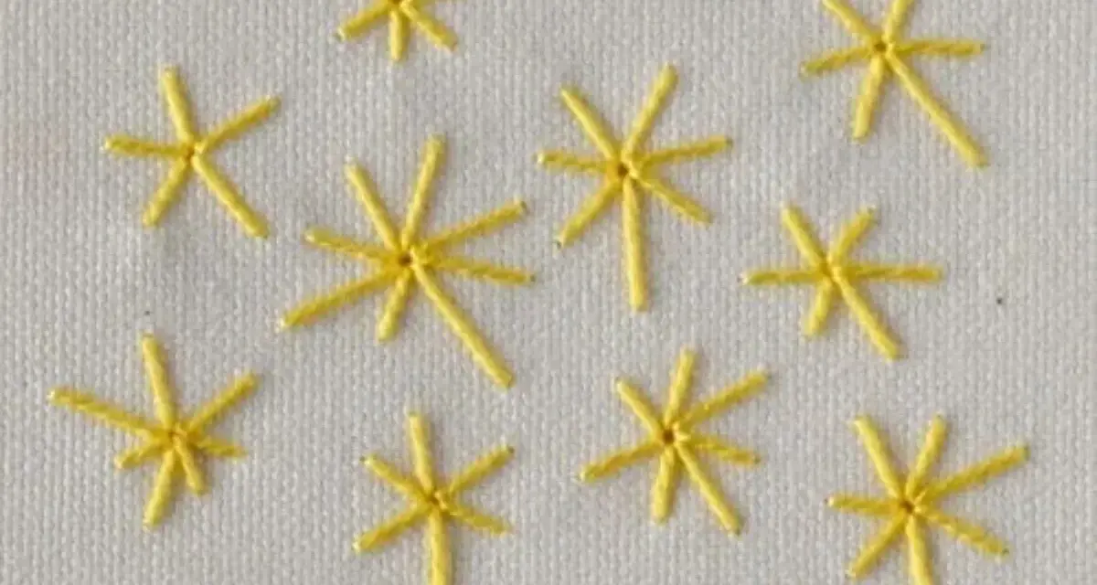 Piccole stelle gialle ricamate a punto pieno su tessuto bianco. Un esempio di come ricamare una stella a punto pieno.