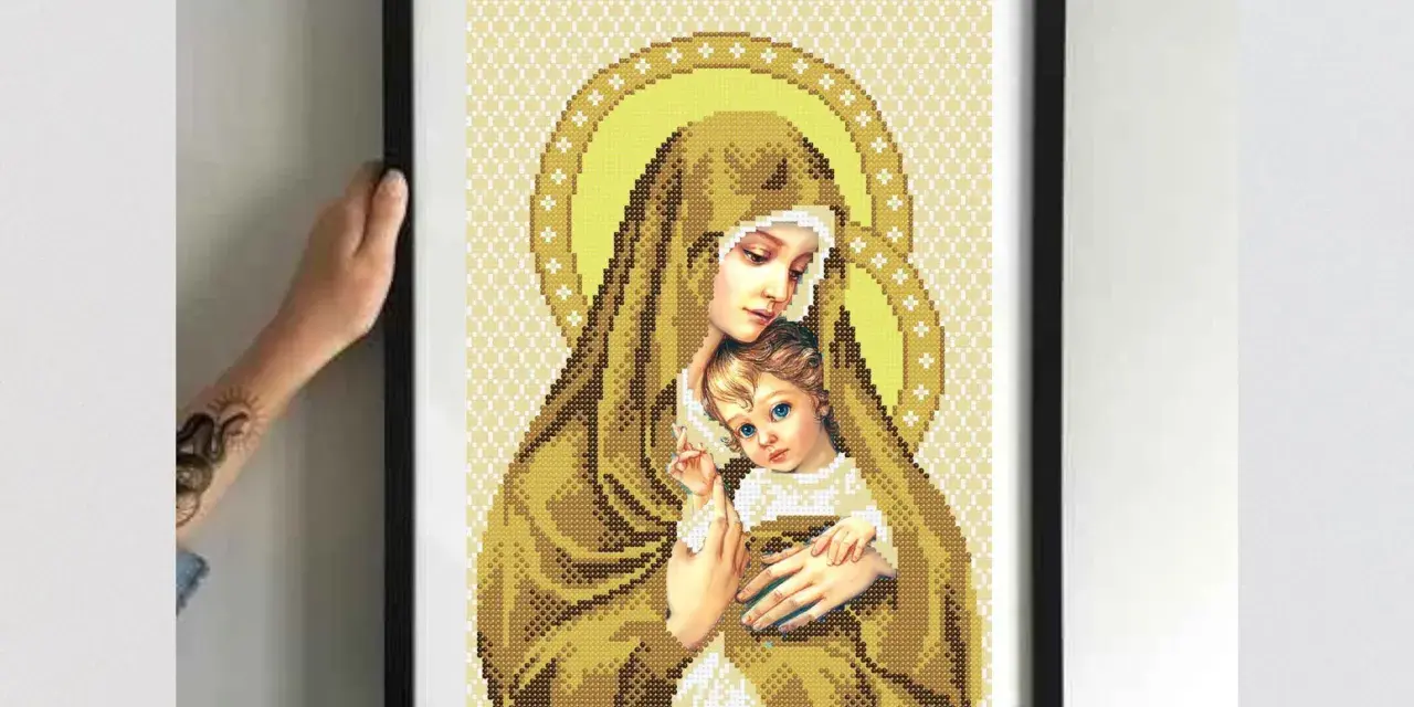 Cross-stitch of Madonna and Child in a black frame, held by hands.
