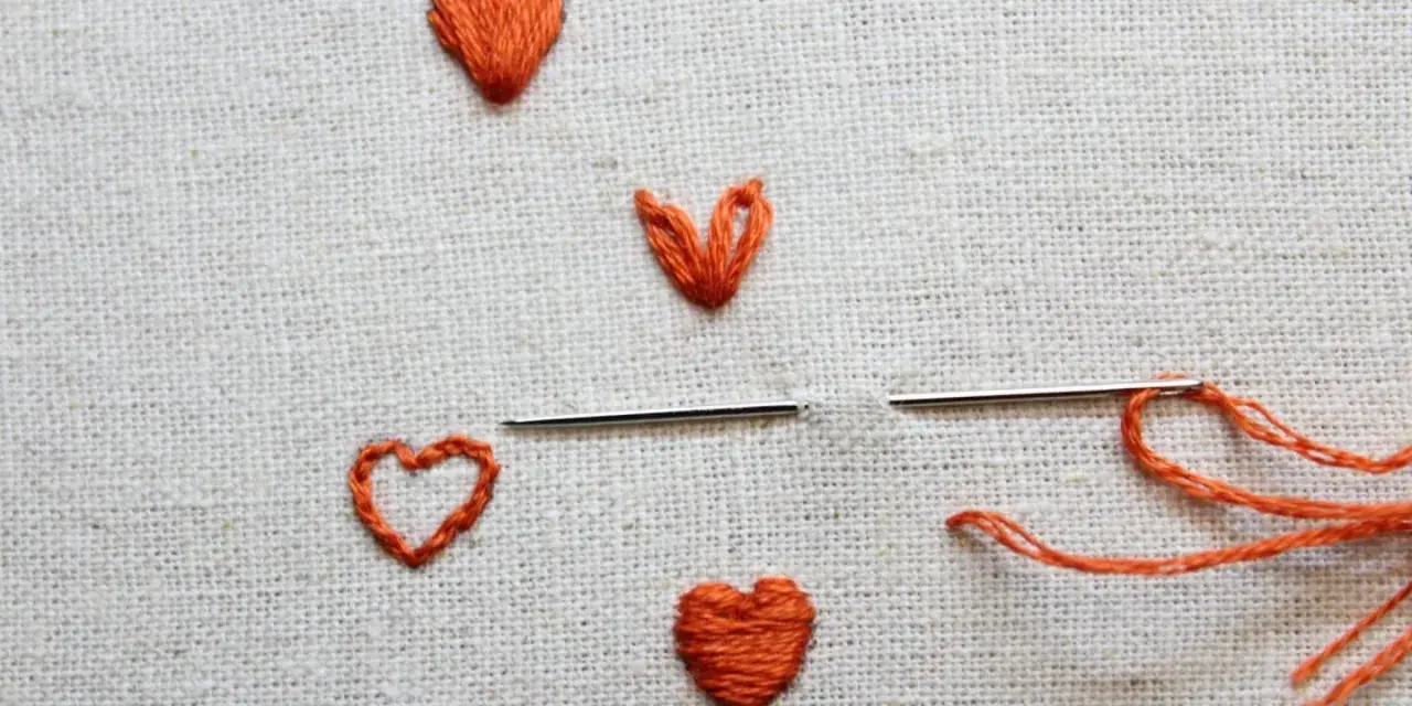 Un ago con filo arancione pronto per creare un altro cuore ricamato a mano su tela grezza.