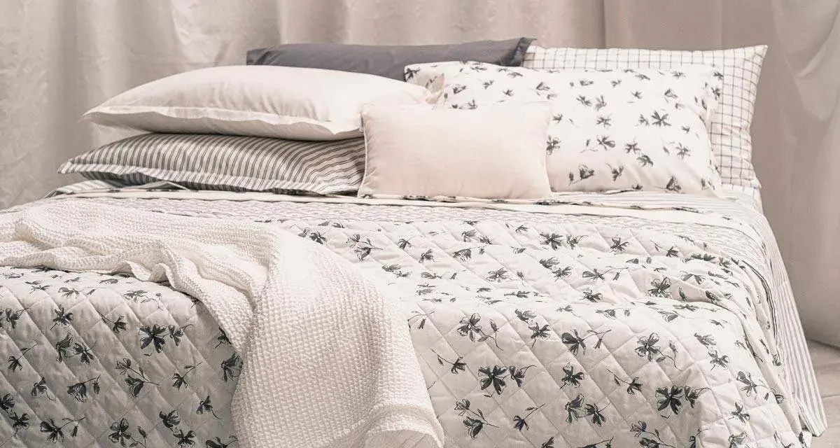 Un letto accogliente con biancheria a fiori e righe, coperte morbide e cuscini che invitano al riposo, come in un sogno di letti all'americana.