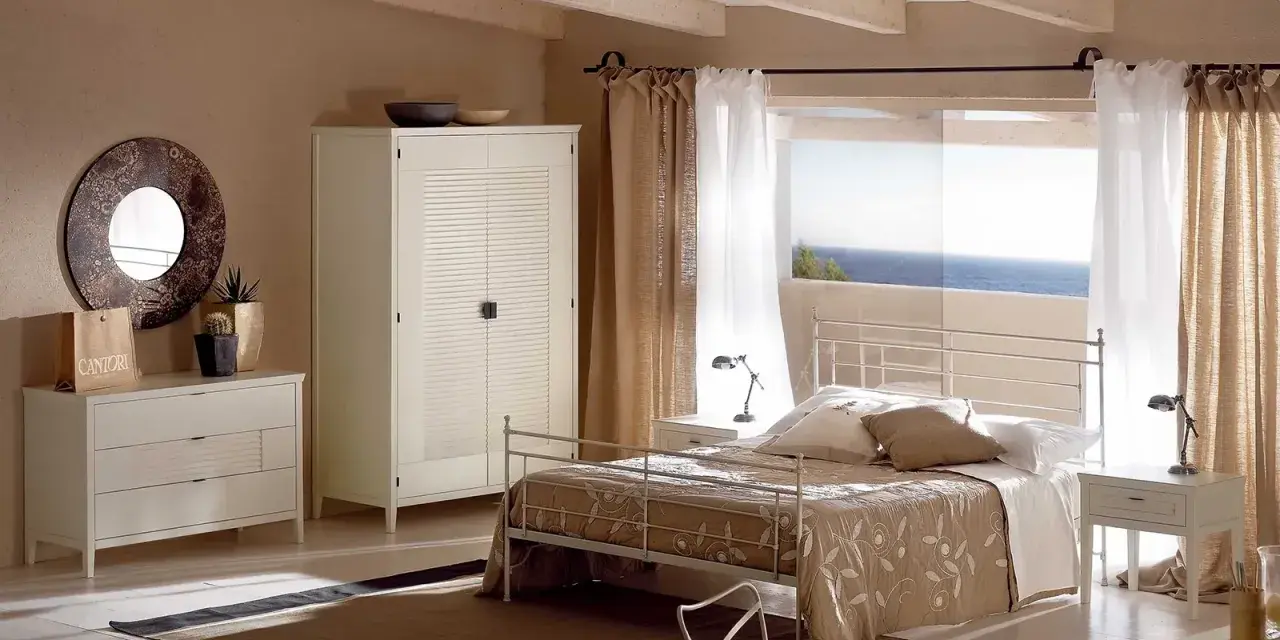 Camera da letto con letto tortora, armadio bianco e cassettiera. Abbinamenti eleganti per un ambiente rilassante con vista mare.