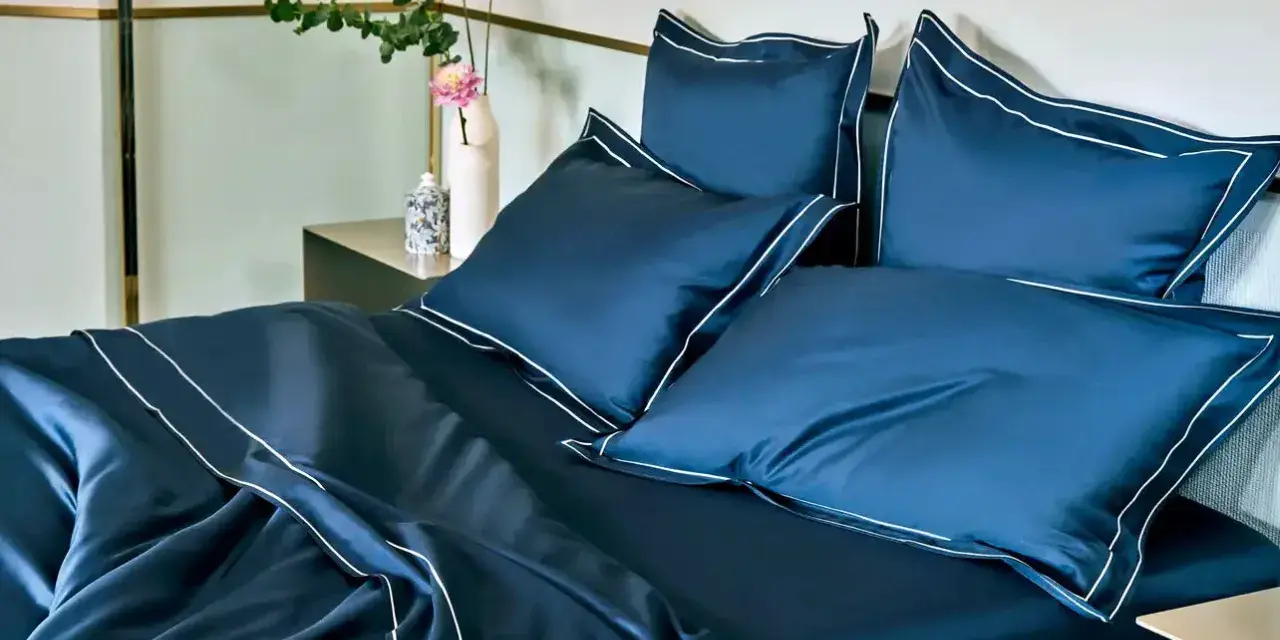 Letto matrimoniale con copriletto blu scuro e cuscini coordinati, rifiniti con bordi bianchi. Ideale per conoscere le misure copriletto matrimoniale.