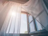 Tende leggere e ariose, fissate senza fare buchi, fluttuano dolcemente con la brezza che entra da una finestra aperta, illuminata dal sole.