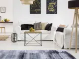 Un soggiorno moderno con divani bianchi, un tavolino in legno e metallo, e un tappeto grigio e nero che sembra pronto per essere lavato.