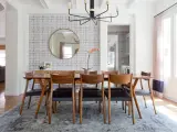 Tavolo da pranzo in legno con sedie in pelle nera, tappeto sotto il tavolo da pranzo si, con carta da parati a motivi geometrici e specchio rotondo.