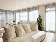 Soggiorno luminoso con divano beige e tende che non fanno vedere dall'esterno, creando un'atmosfera intima.