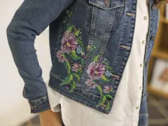 Giacca di jeans con un bellissimo ricamo su stoffa di fiori colorati e foglie verdi.