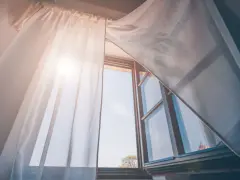 Tende leggere e ariose, fissate senza fare buchi, fluttuano dolcemente con la brezza che entra da una finestra aperta, illuminata dal sole.