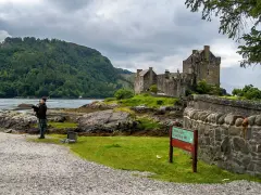 Uomo con cornamusa indossa un kilt scozzese davanti a un castello.