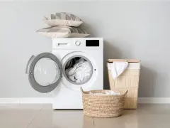 Lavatrice con oblò aperto, piena di biancheria. Sopra, due cuscini decorativi. Accanto, cesti per la biancheria. Il peso dei lenzuola matrimoniali non è un problema per questa lavatrice.