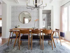 Tavolo da pranzo in legno con sedie in pelle nera, tappeto sotto il tavolo da pranzo si, con carta da parati a motivi geometrici e specchio rotondo.