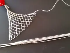 Un ago con filo bianco e un pezzo di rete a maglie, un tipo di ricamo eseguito su una rete a maglie, con un nastro rosso in alto.