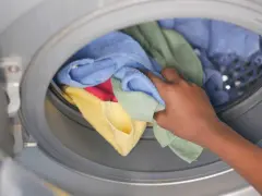 Mano inserisce asciugamani colorati in lavatrice. Scopri come lavare asciugamani in lavatrice per mantenerli morbidi e profumati.