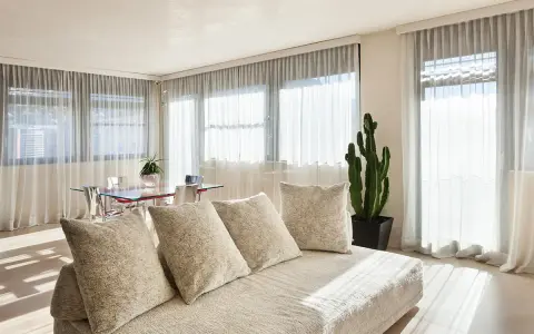 Soggiorno luminoso con divano beige e tende che non fanno vedere dall'esterno, creando un'atmosfera intima.
