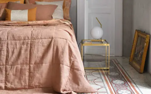 Un morbido quilt matrimoniale color pesca, con cuciture a quadri, adorna un letto in una stanza elegante.