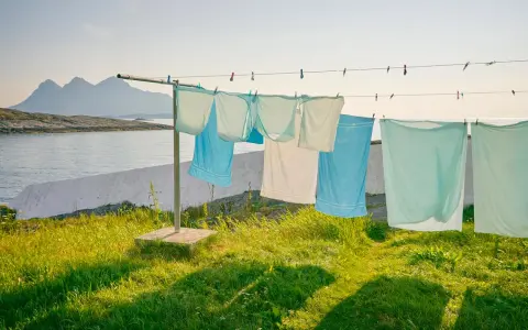 Magliette stese al sole su un filo, con montagne e mare sullo sfondo. Un modo naturale per stendere le magliette per non stirarle.