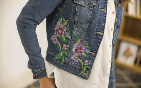 Giacca di jeans con un bellissimo ricamo su stoffa di fiori colorati e foglie verdi.