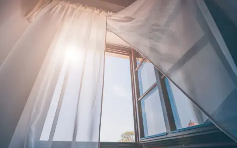 Tende leggere e ariose, fissate senza fare buchi, fluttuano dolcemente con la brezza che entra da una finestra aperta, illuminata dal sole.