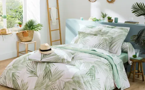 Un letto preparato per l'estate con biancheria a tema tropicale, un cappello di paglia e una borsa di vimini.