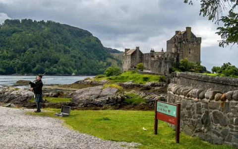 Uomo con cornamusa indossa un kilt scozzese davanti a un castello.
