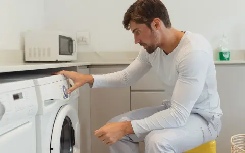 Uomo in pigiama imposta la lavatrice per asciugare la ciniglia.