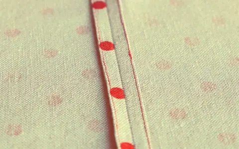 Tessuto a pois rossi con cucitura a vista, un punto per rifinire bordi con precisione sartoriale.
