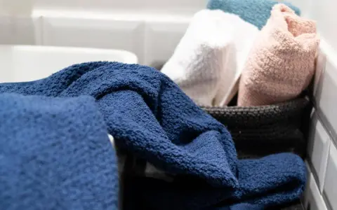 Asciugamani spugna blu, bianchi, rosa e azzurri in un cesto. Il primo lavaggio li rende ancora più soffici e pronti all'uso.