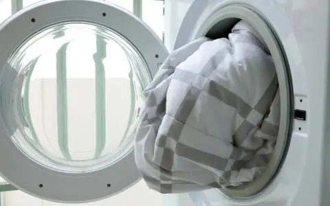 A white and grey checkered duvet being loaded into a washing machine.