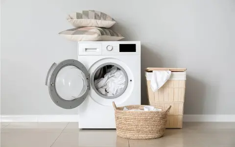 Lavatrice con oblò aperto, piena di biancheria. Sopra, due cuscini decorativi. Accanto, cesti per la biancheria. Il peso dei lenzuola matrimoniali non è un problema per questa lavatrice.