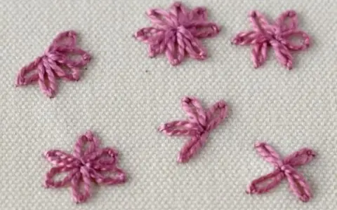 Close-up of five small, pink embroidered daisy stitches on a cream fabric background.