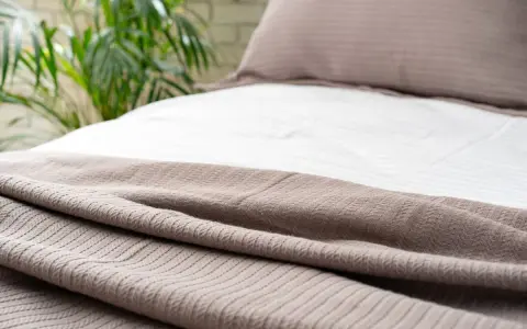 Un morbido copripiumino color tortora, con un motivo a rombi, adorna un letto con lenzuola bianche a righe.