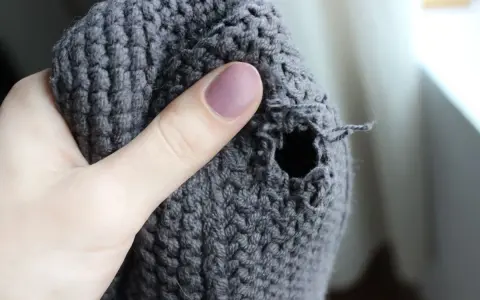 Dito un buco in un maglione grigio, pronto per imparare come rammendare uno strappo a mano.