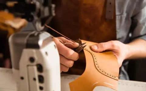 Mani esperte che cuciono la pelle con filo e ago, creando un dettaglio decorativo su un pezzo di cuoio.