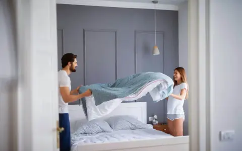 Coppia felice che cambia le lenzuola, un gesto che ci ricorda ogni quanto cambiare le lenzuola per un sonno più sano.